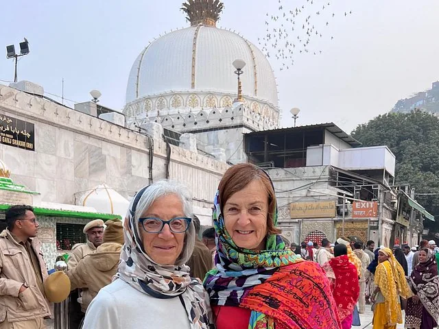 Two women wearing headscarves standing in front of a white domed shrine.