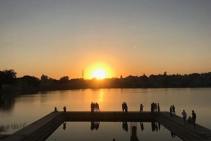 People silhouetted against a sunset over a calm lake.