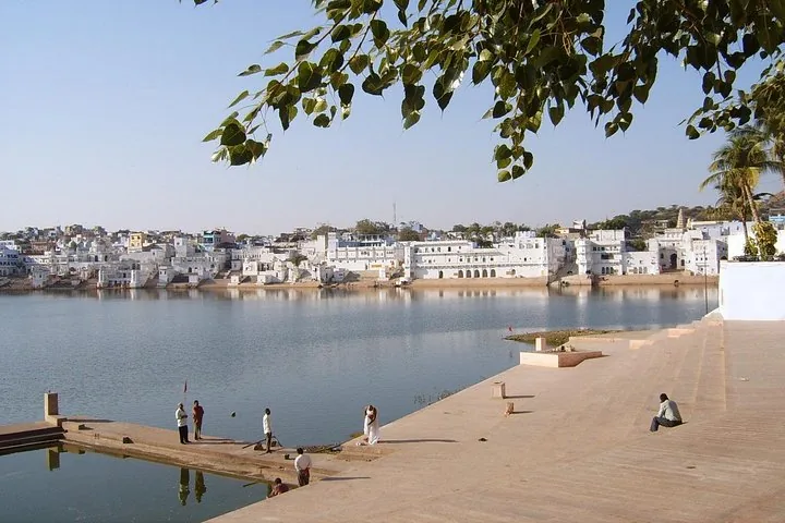 People near a large body of water with white buildings in the background.
