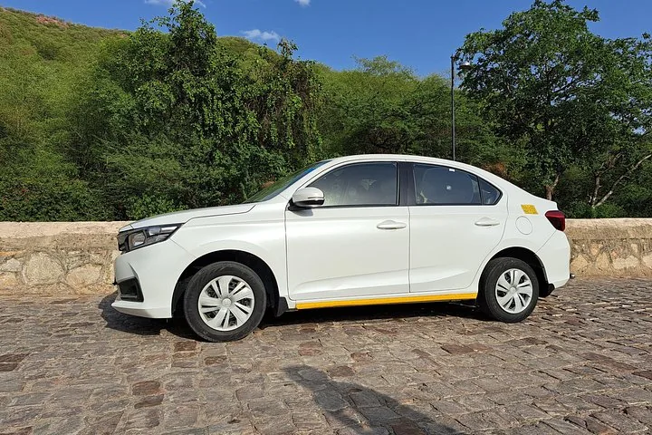 A white car parked on a stone path near hills.